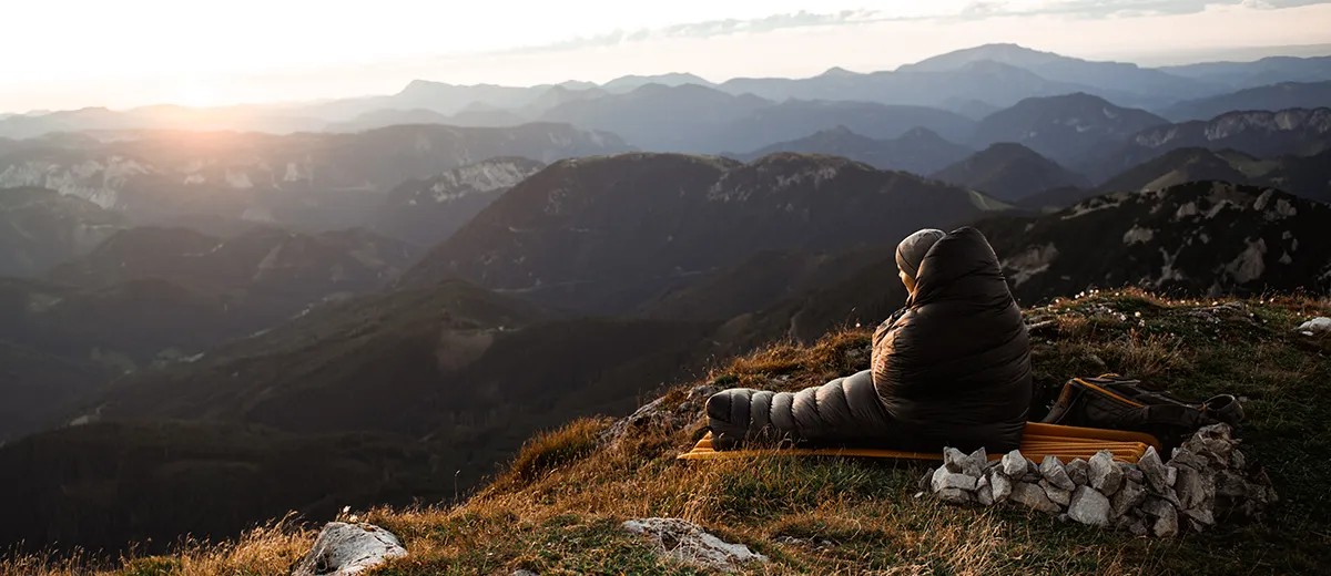 Person sitzt im Gr�ezi bag DownWool 2.0 Schlafsack beim Sonnenaufgang in den Alpen